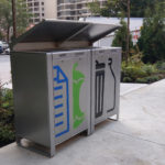 Trois poubelles extérieures étiquetées pour le papier, le compost et les déchets, placées sur un trottoir à proximité de verdure et de voitures garées dans une zone urbaine.
