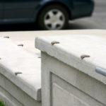 Concrete ledges with metal skate-stoppers installed along the edges, next to a sidewalk and grass, with part of a parked car visible in the background.