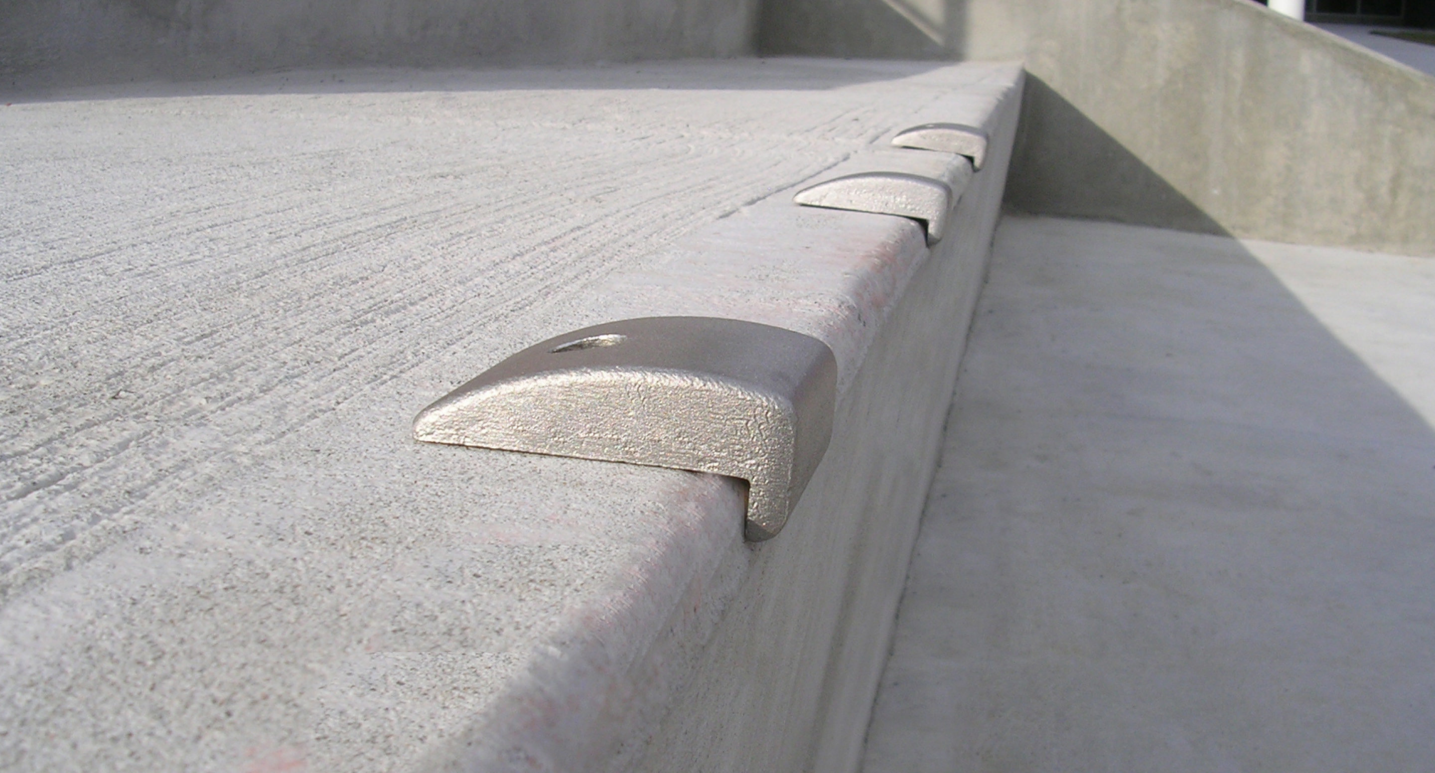 maglin_mac-0300-wall-mount-skate-deterrents-2 Close-up of a concrete ledge with several evenly spaced metal skate deterrents installed along the edge.