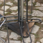Close-up view of metal chair legs and a table base on a stone-paved ground with patches of grass.