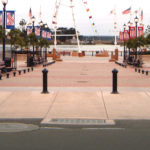 Une allée pavée bordée de bancs, d'arbres, de lampadaires et de bannières patriotiques mène à un plan d'eau où flottent plusieurs drapeaux américains.