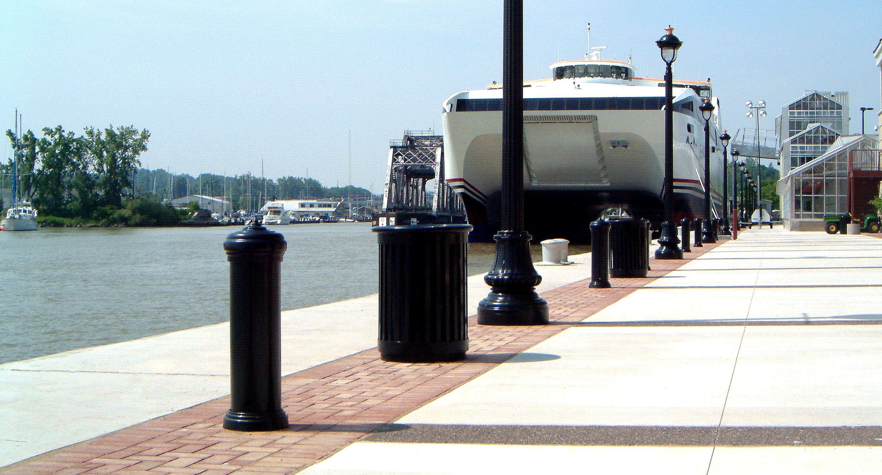 maglin_mbo-0200-bollards-1 Un ferry accoste à un quai situé à côté d'une passerelle bordée de bornes noires et de lampadaires par une journée ensoleillée.