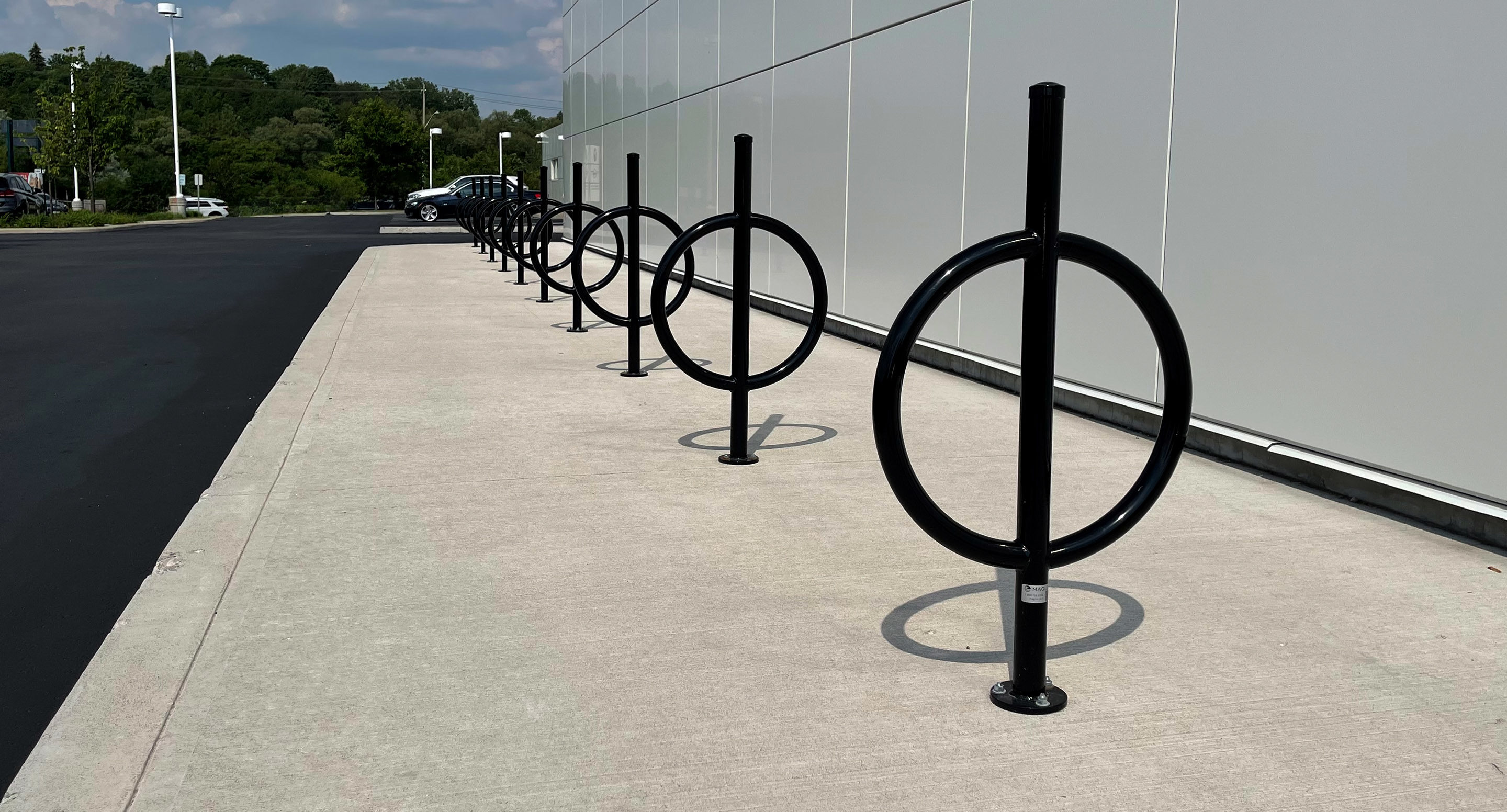 A row of black metal bicycle racks with circular designs is installed on a concrete sidewalk next to a modern building.