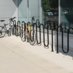 Several bicycles are parked and locked to black metal bike racks outside a modern building with large windows.