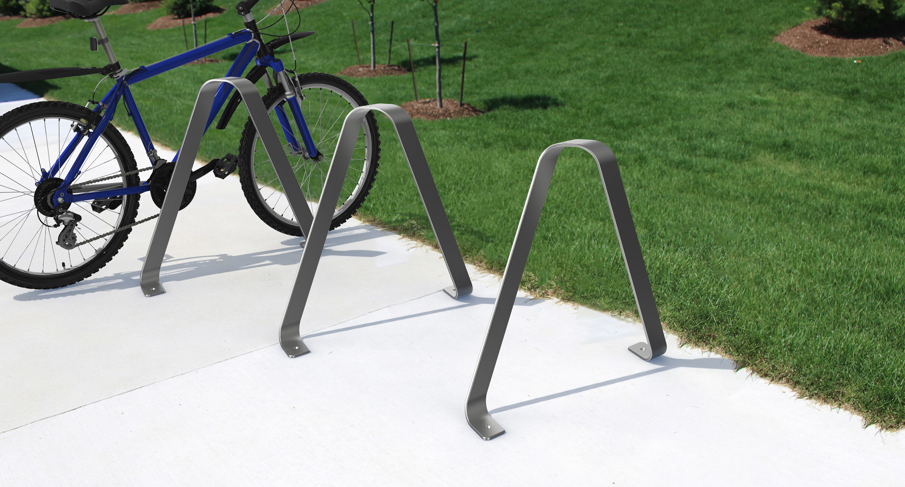 maglin_mbr-3100-bike-racks-hero A blue bicycle is parked in a metal bike rack on a concrete walkway next to a grassy lawn with small plants and mulch.