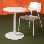 A white round table and a matching white chair are placed on a green carpet against an orange wall.