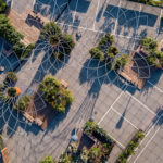Aerial view of a parking lot converted into an urban garden with geometric wire structures, benches, and greenery arranged in patterned sections.