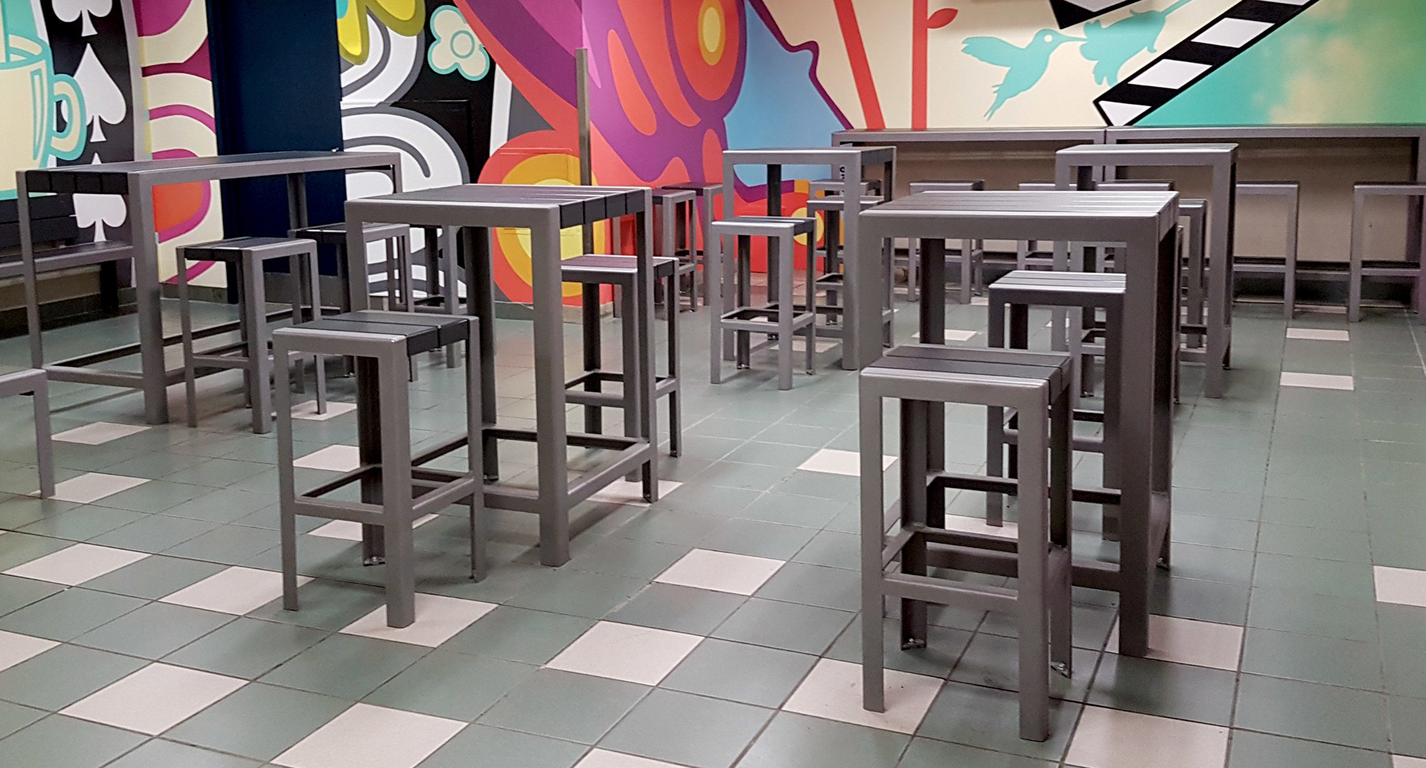 maglin_mtb-1050-bar-height-tables-2 A cafeteria with high square tables and stools on a tiled floor, featuring a colorful mural on the back wall.