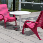 Deux chaises roses à barreaux et une table ronde blanche sont placées sur un patio extérieur carrelé.