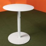 A round, white pedestal table stands on a green floor against orange walls.