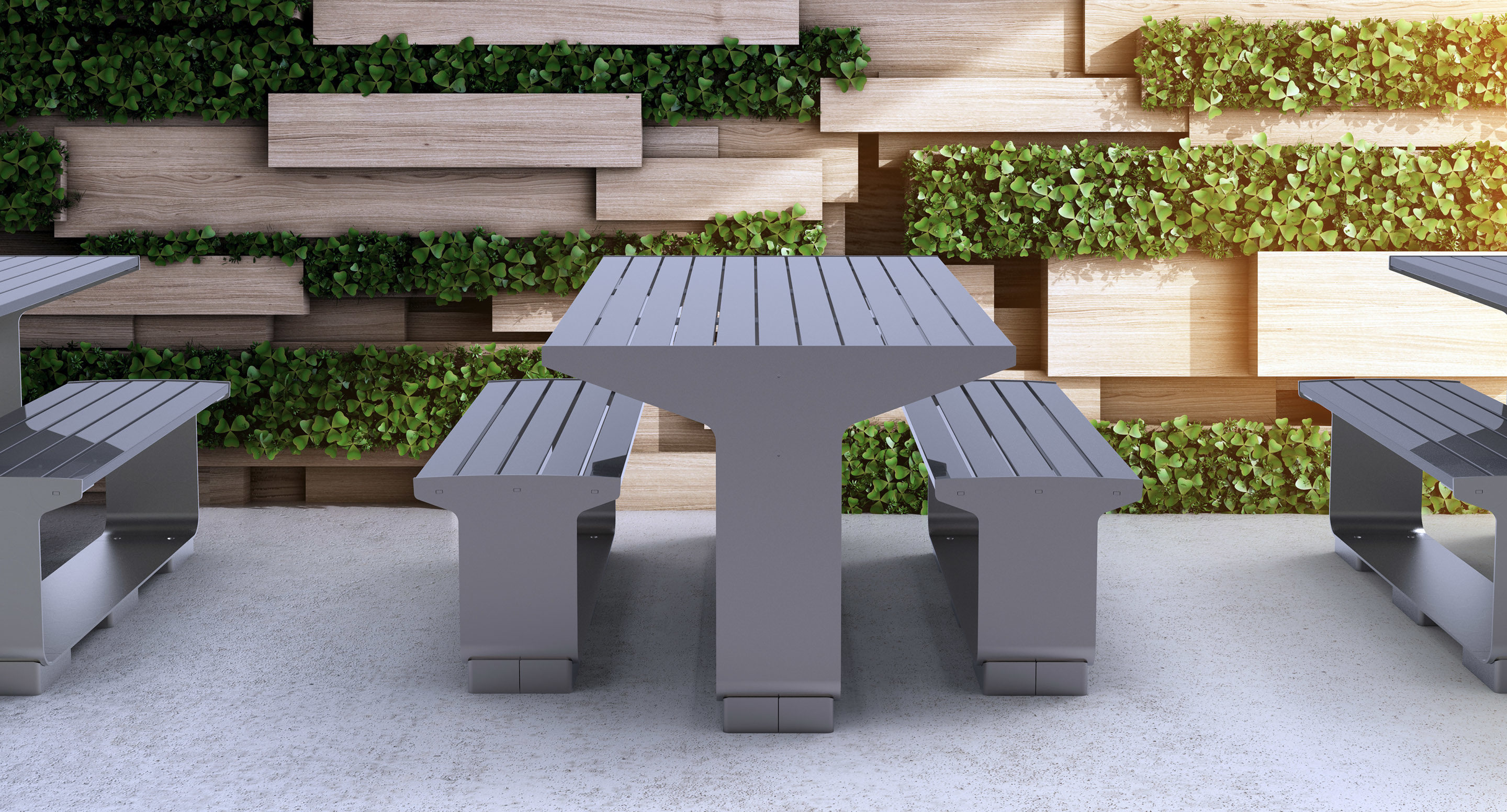 maglin_mtb-3000-l-series-tables-4 Gray metal outdoor table with benches on a concrete surface, placed in front of a decorative wall featuring wooden panels and green plants.