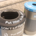 Two outdoor bins side by side: a black trash bin labeled