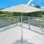 Un parasol blanc se trouve sur un balcon carrelé avec des balustrades en verre transparent, surplombant des arbres verts et un ciel bleu avec des nuages épars.
