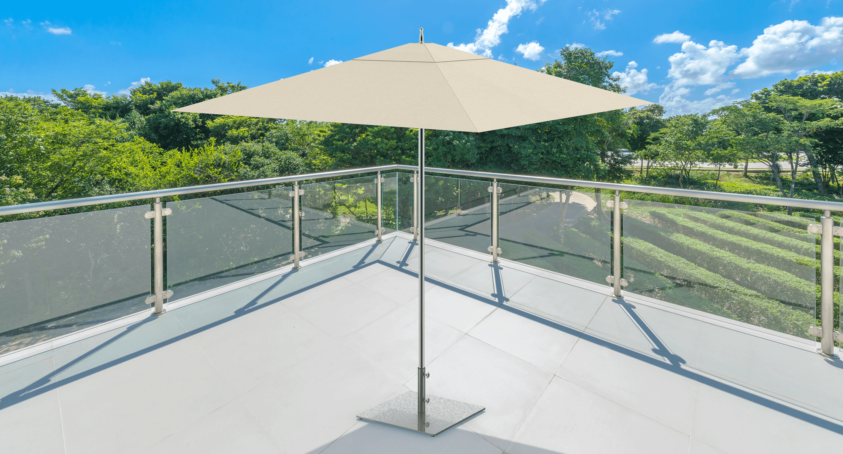 maglin_mum-2400-square-umbrella-base Un parasol blanc se trouve sur un balcon carrelé avec des balustrades en verre transparent, surplombant des arbres verts et un ciel bleu avec des nuages épars.