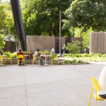 Students and visitors eat lunch, study, and relax at Battery Tables with Aries Café Chairs, showing the social benefits of movable seating in a thoughtful campus design; surrounded by trees and modern structures on a sunny day.