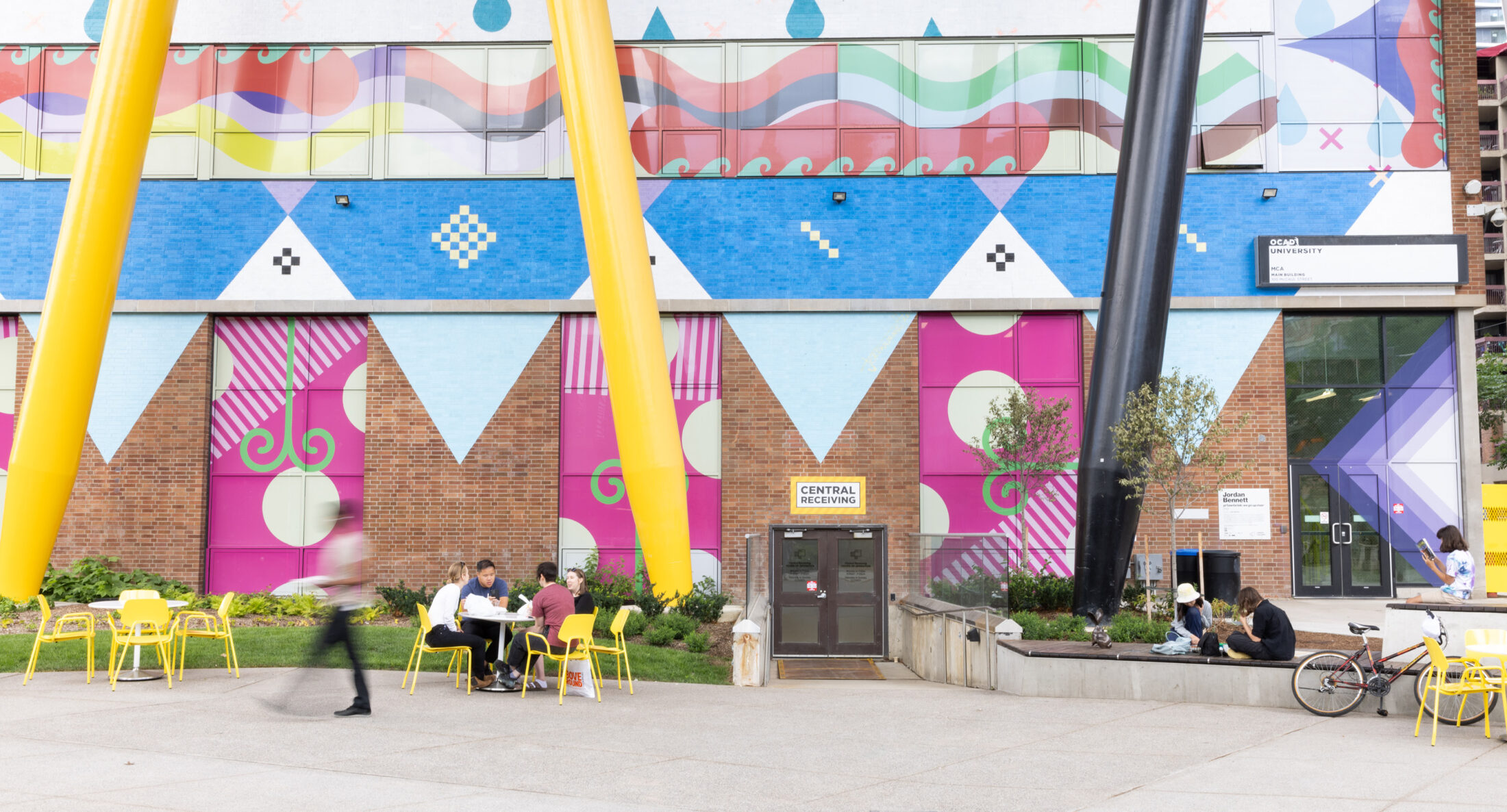 Wide view of movable seating at OCAD University’s Butterfield Park, with yellow Aries Café Chairs and Battery Tables under the iconic Sharp Centre for Design.