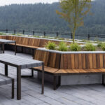 Un patio sur le toit de la Collection Ogden, avec des bancs en bois, des jardinières et des tables en métal, donne sur une colline boisée en arrière-plan.