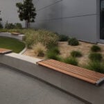 Curved concrete with backless 720 wall-mount benches in a landscaped outdoor area next to a modern building, surrounded by grass, shrubs, and small trees.