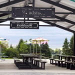 Covered outdoor picnic area with wooden tables, benches, colorful umbrellas, and a sign reading 