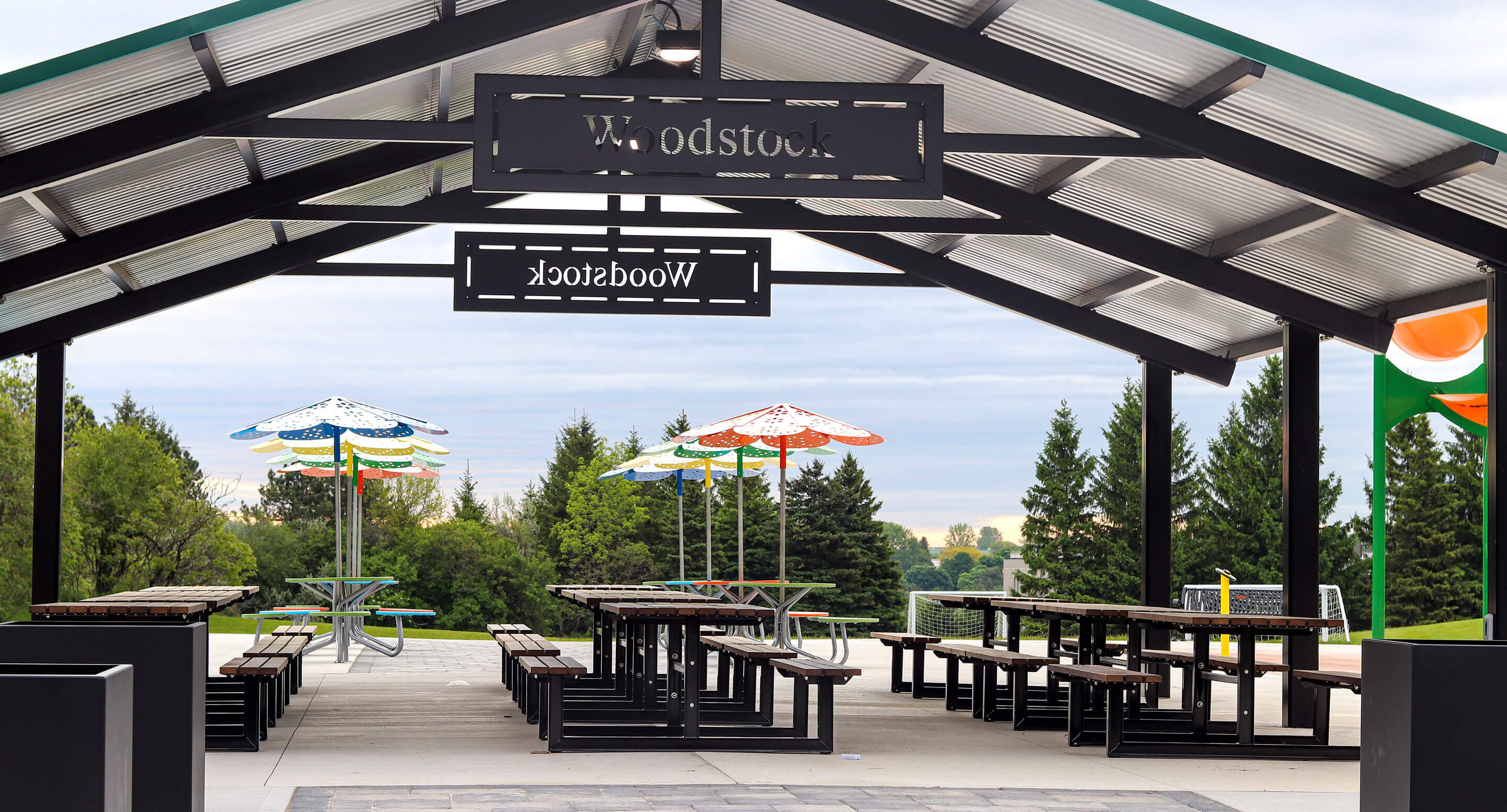 Covered outdoor picnic area with wooden tables, benches, colorful umbrellas, and a sign reading 