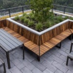 Rooftop patio with wooden benches, metal tables, and a central raised planter with greenery, surrounded by glass railing and overlooking a forested area.