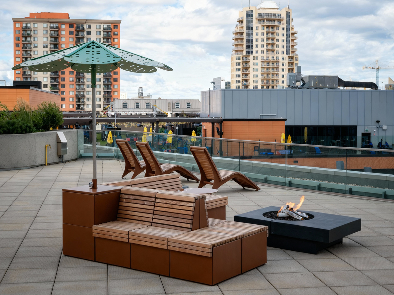 A rooftop patio features modern wooden site furniture, a metal shade structure, a fire pit, lounge chairs, and a cityscape backdrop with tall buildings—showcasing thoughtful space planning.