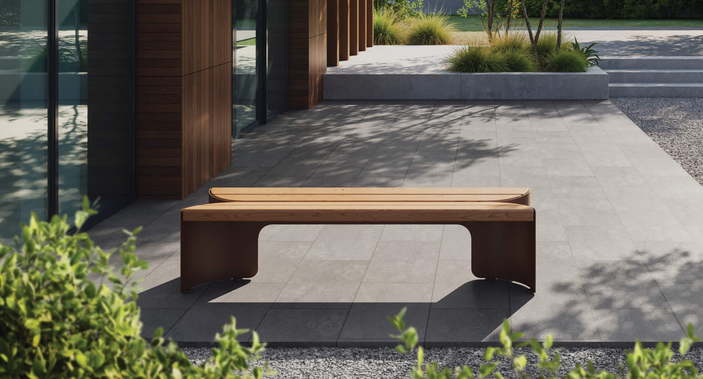 Un banc moderne en bois est posé sur un patio carrelé à l'extérieur d'un bâtiment avec des panneaux en bois, entouré de plantes et de verdure - un endroit accueillant qui rappelle les designs récompensés par les prix A+, parfait pour se détendre ou présenter de charmants jouets Corolle.