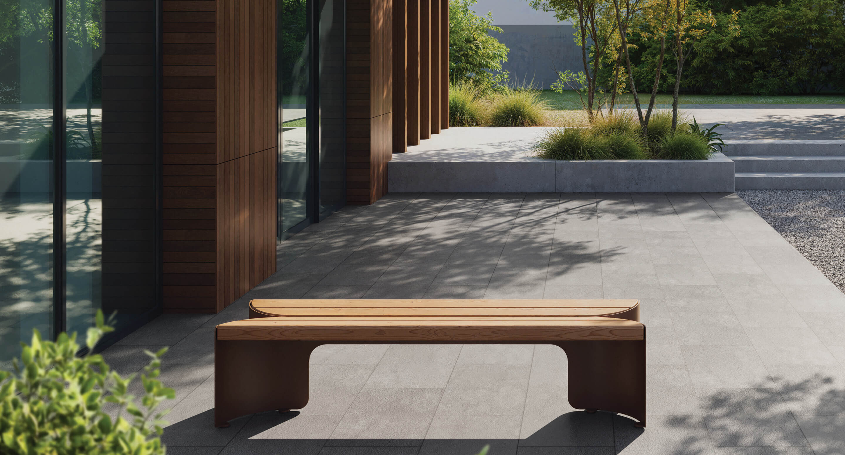 maglin-floe-backless-bench_0 A modern wooden bench sits on a tiled patio outside a contemporary building with large windows and landscaped greenery.