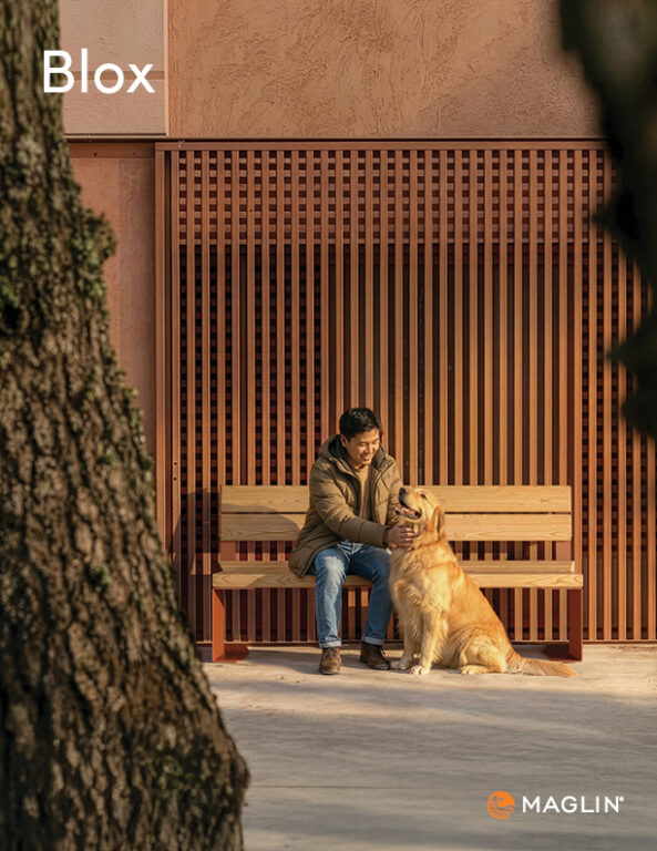 Une personne est assise sur un banc en bois à côté d'un golden retriever devant un mur en lattes, avec des arbres partiellement visibles au premier plan.