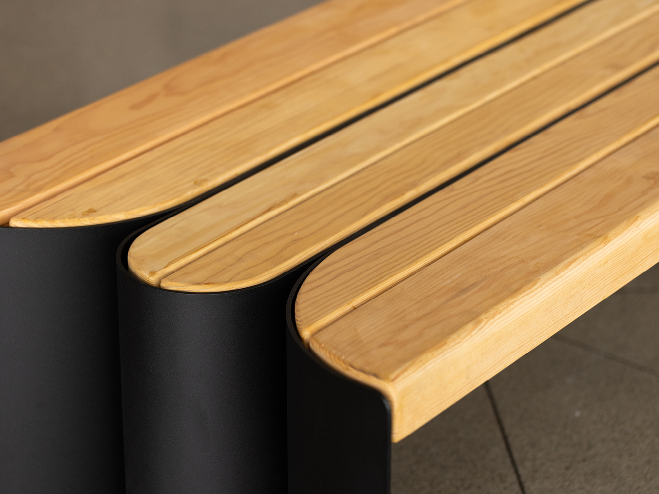 Close-up view of a modern bench with Douglas Fir wood slats and black metal sides on a tiled floor.