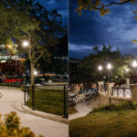 A city park at night with lit street lamps, benches, winding concrete paths, and trees; the National War Memorial of Newfoundland rises in the background alongside buildings and parked cars.