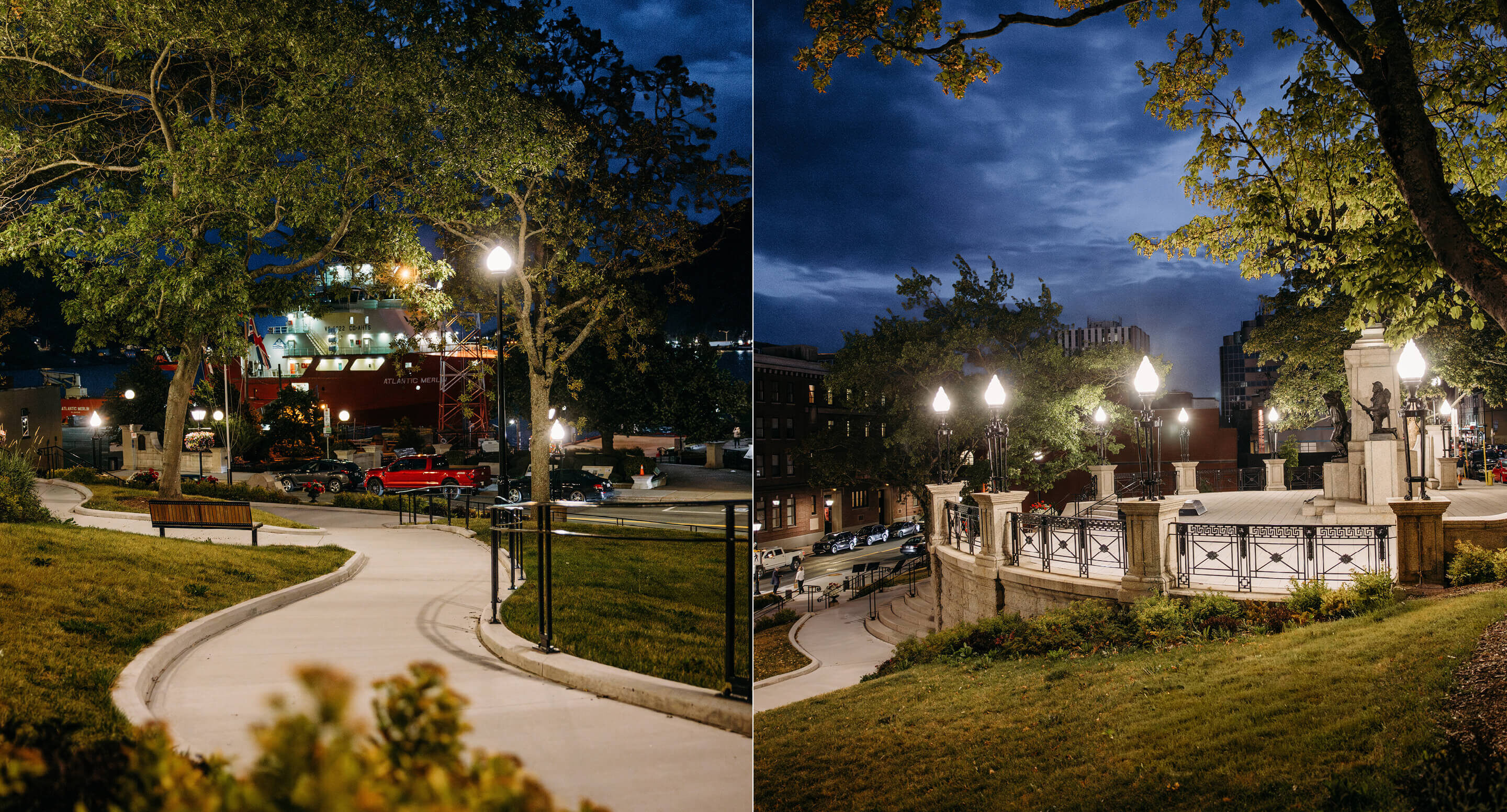 A city park at night with lit street lamps, benches, winding concrete paths, and trees; the National War Memorial of Newfoundland rises in the background alongside buildings and parked cars.