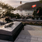 The Tomb of the Unknown Soldier, part of the National War Memorial in Newfoundland, stands on a set of steps overlooking a river, with Canadian and British flags and a sunset in the background.