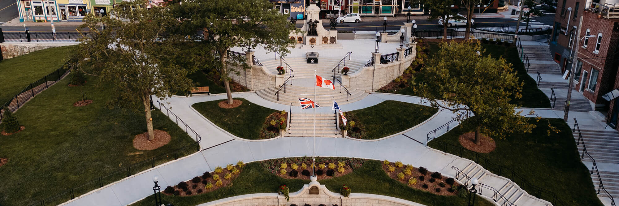 Vue aérienne d'une place publique aménagée avec des drapeaux, des monuments et des escaliers, entourée de bâtiments colorés et d'espaces verts.