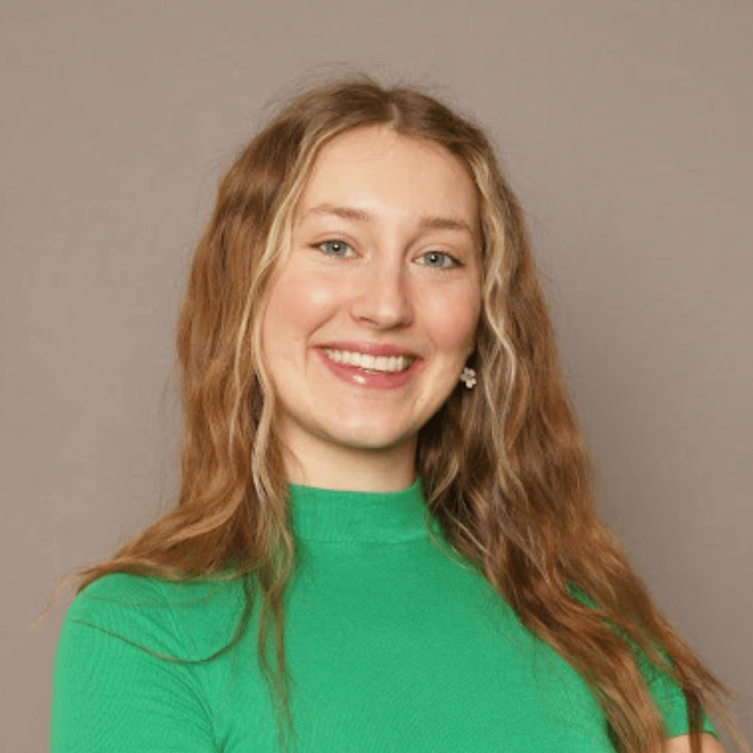 A woman with long wavy blonde hair, wearing a green top, smiles at the camera against a plain beige background.