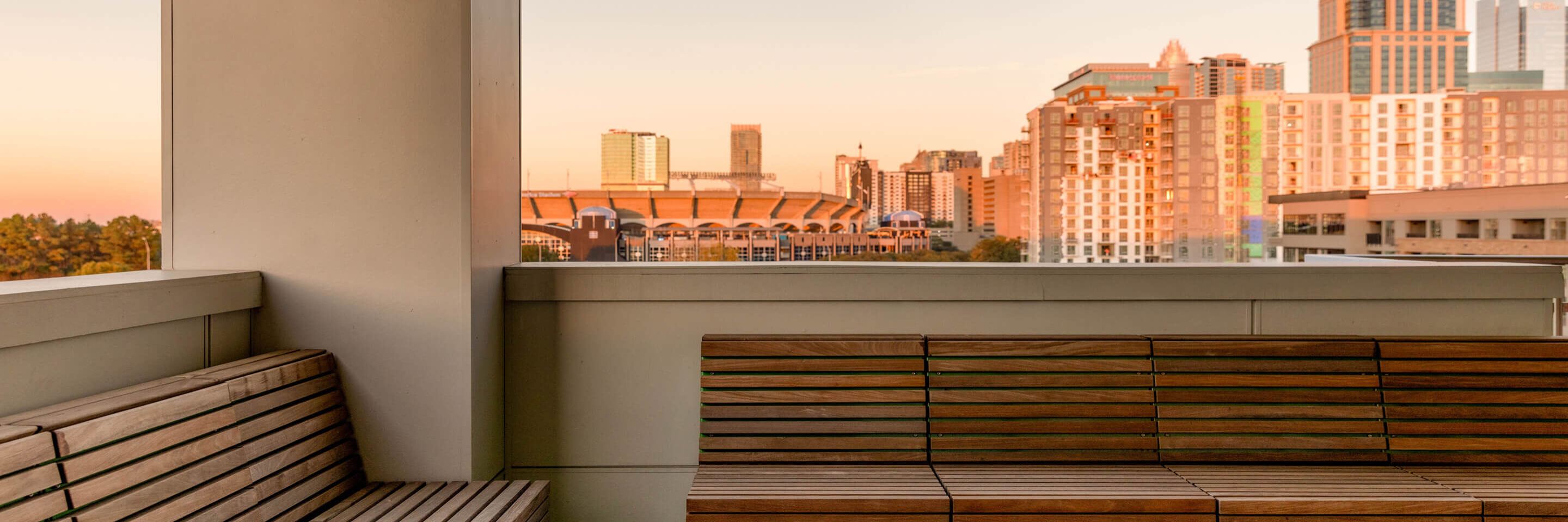 Outdoor seating area with wooden Pixel Collection benches and green bases, overlooking a city skyline with tall buildings during sunset.