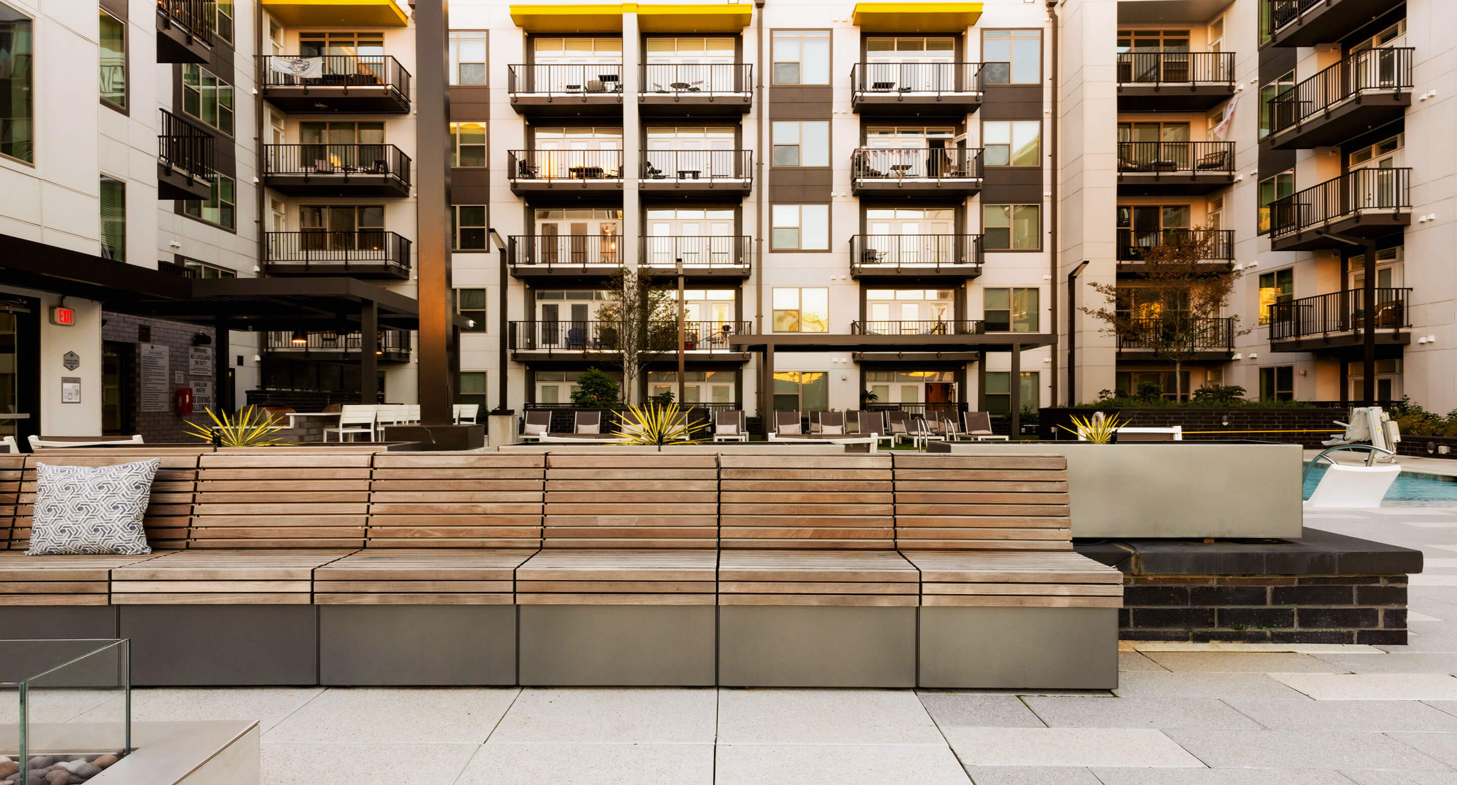 Modern apartment courtyard at Link Apartments Mint Street in Charlotte, NC, featuring wooden benches, planters, and a pool area, all surrounded by multi-story buildings with balconies.