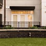 Curved wooden bench on artificial grass in front of a modern apartment building with white patio doors and railings at Link Apartments on Mint Street in Charlotte, NC.