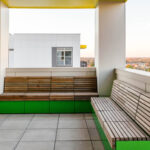 Modern outdoor terrace at Link Apartments, featuring green-base wooden benches, a tiled floor, and a partial cityscape view of Charlotte, NC in the background—ideally situated near Mint Street.