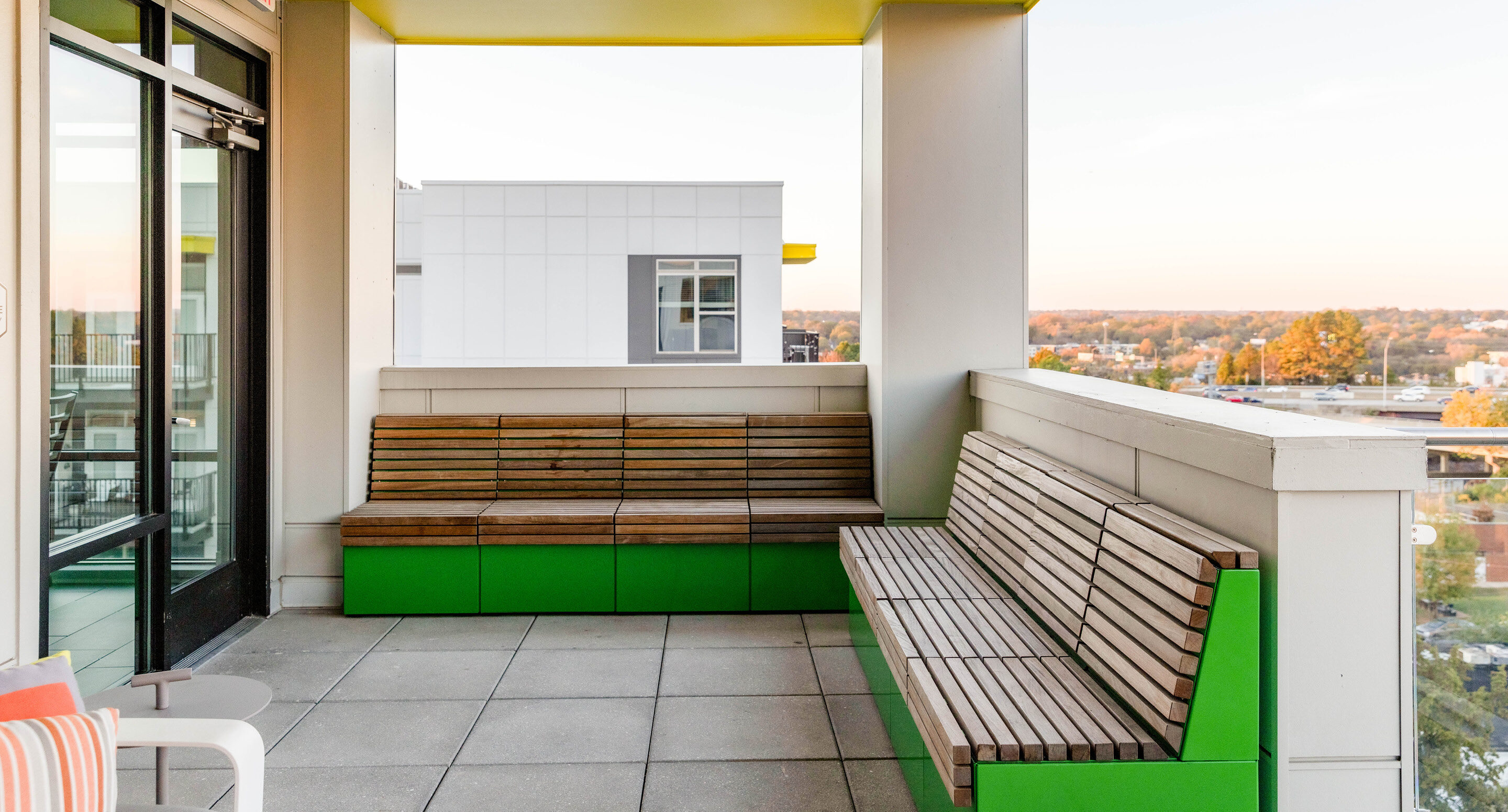 Modern outdoor terrace at Link Apartments, featuring green-base wooden benches, a tiled floor, and a partial cityscape view of Charlotte, NC in the background—ideally situated near Mint Street.