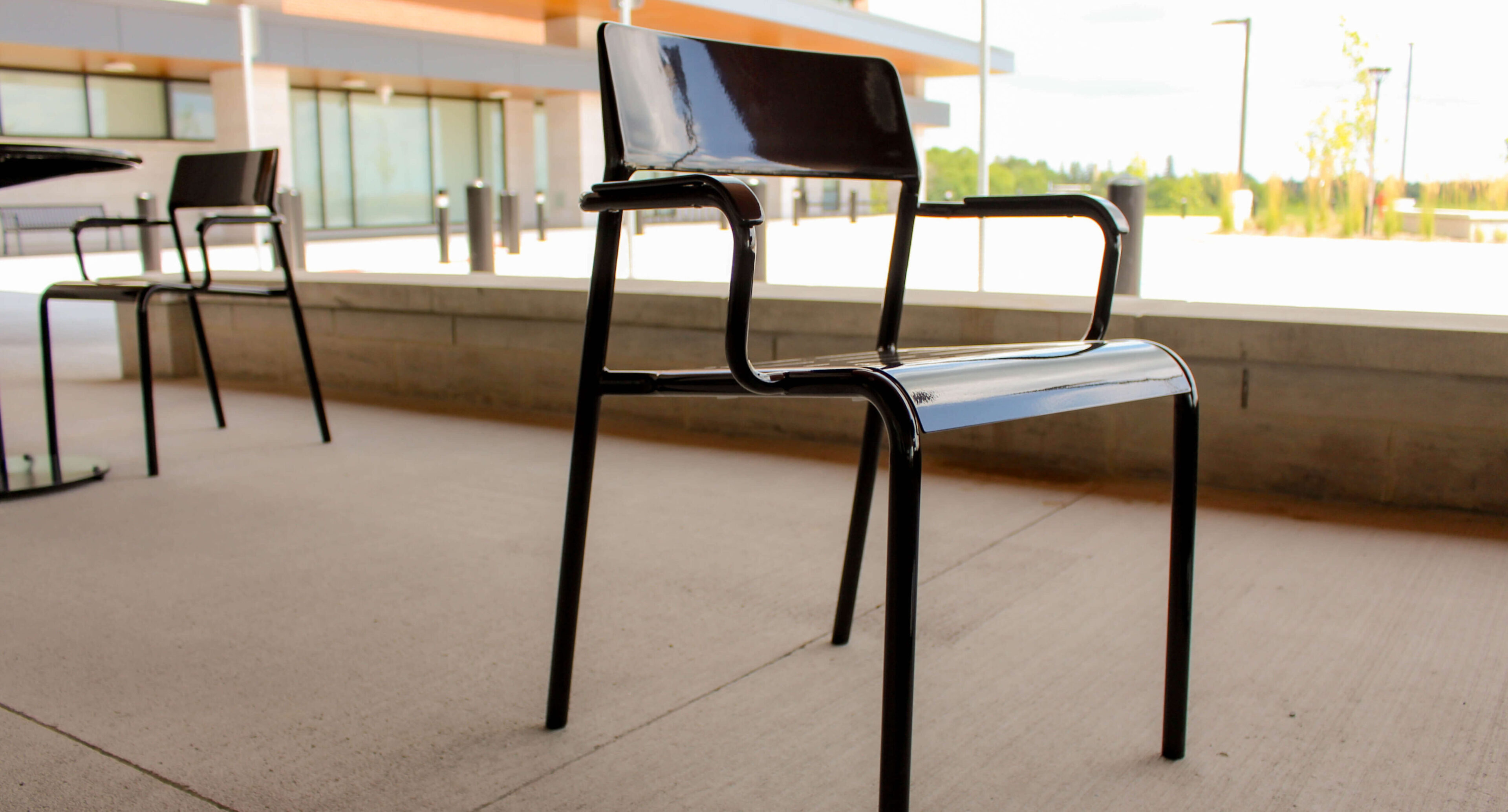 groves-memorial-hospital-foro-chairs-armrests Black metal chair with armrests and a slightly angled backrest placed on a concrete patio outside Groves Memorial Community Hospital’s modern building.