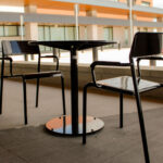 Two black metal chairs and a round table are placed on a concrete outdoor patio at Groves Memorial Community Hospital, with a modern building and windows visible in the background.