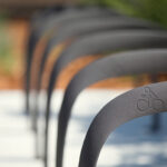 Close-up of a row of metal bicycle racks with a bike symbol engraved on the nearest one, positioned outdoors on a paved surface.