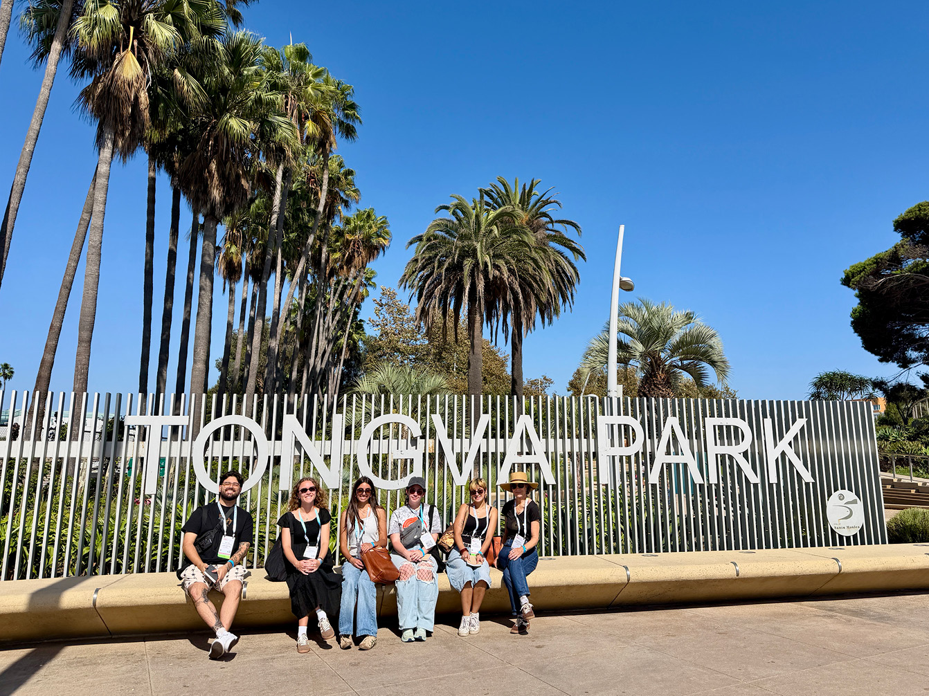 Student Sketch Walk: Six people sit on a bench in front of a Tongva Park sign, with palm trees in the background.