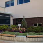 Entrée des urgences, avec trois bancs en bois incurvés placés devant un parterre paysager adossé à la façade du bâtiment.