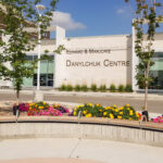 L'extérieur du bâtiment du Centre Edward & Marjorie Danylchuk, avec au premier plan un banc en bois incurvé et des parterres de fleurs.