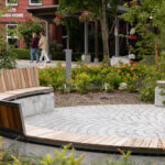Un banc incurvé en bois et en béton entourant un patio circulaire en pierre dans un parc.