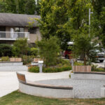 Deux bancs circulaires en béton avec des assises en bois dans un parc, avec un immeuble d'habitation en arrière-plan.