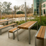 Terrasse extérieure équipée de plusieurs tables et bancs en bois, aménagée sur une esplanade en béton à côté d'un bâtiment aux façades vitrées.
