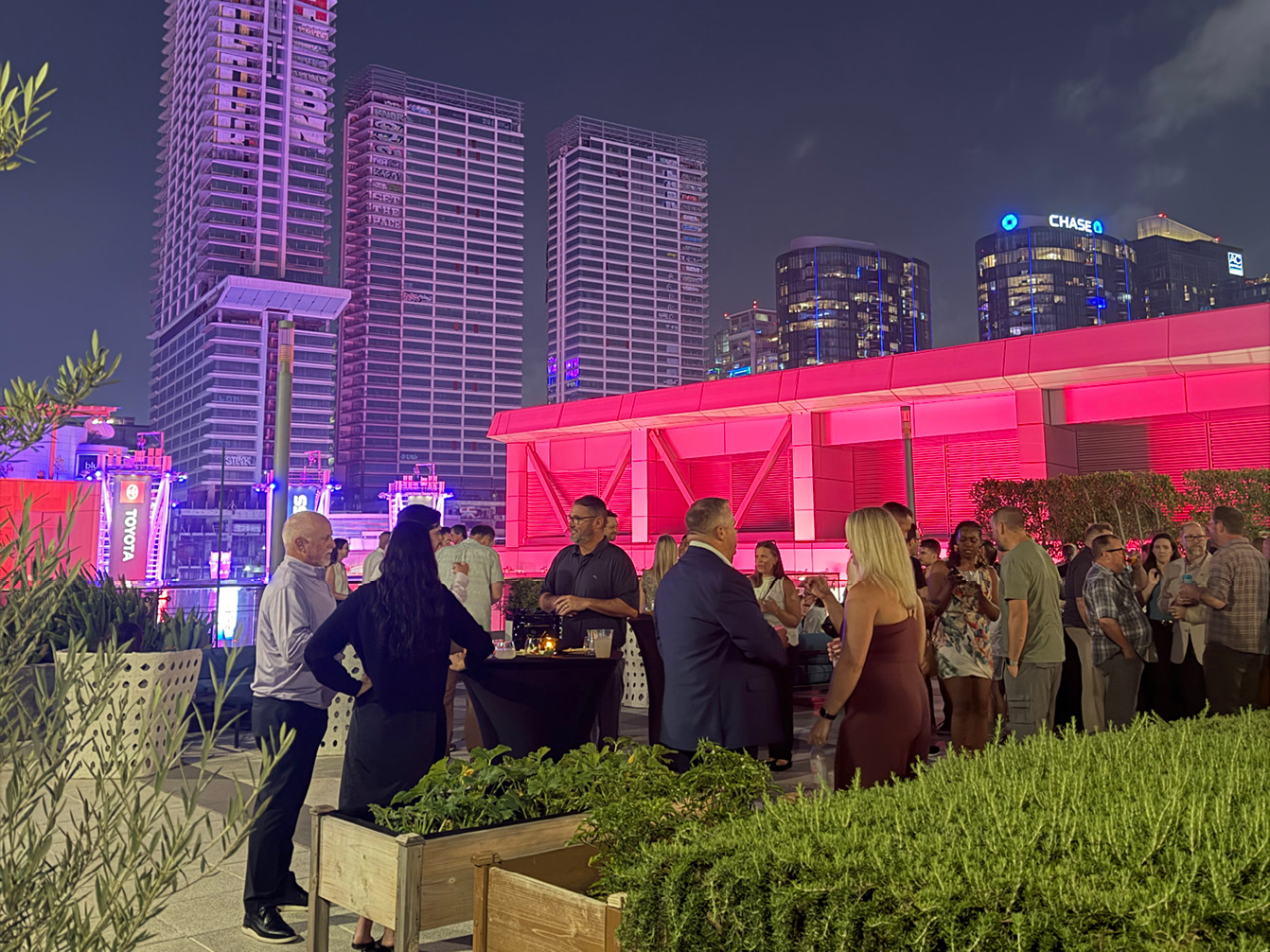 People socializing at an outdoor rooftop event designed with Maglin landscape architecture, set against a backdrop of illuminated city skyscrapers at night.